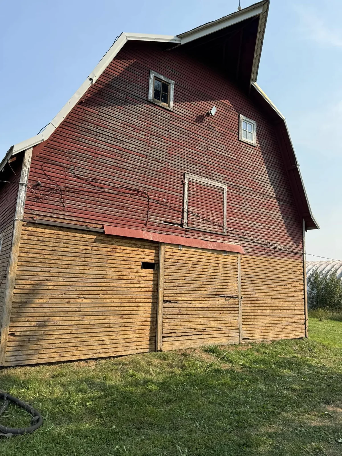 Barn gable mid-strip — red paint lifting off, golden original wood emerging below